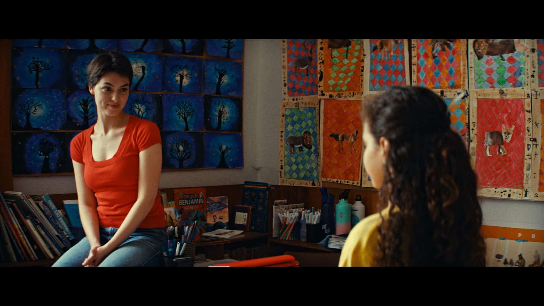 Une femme et une jeune fille se font face dans une salle décorée de dessins.