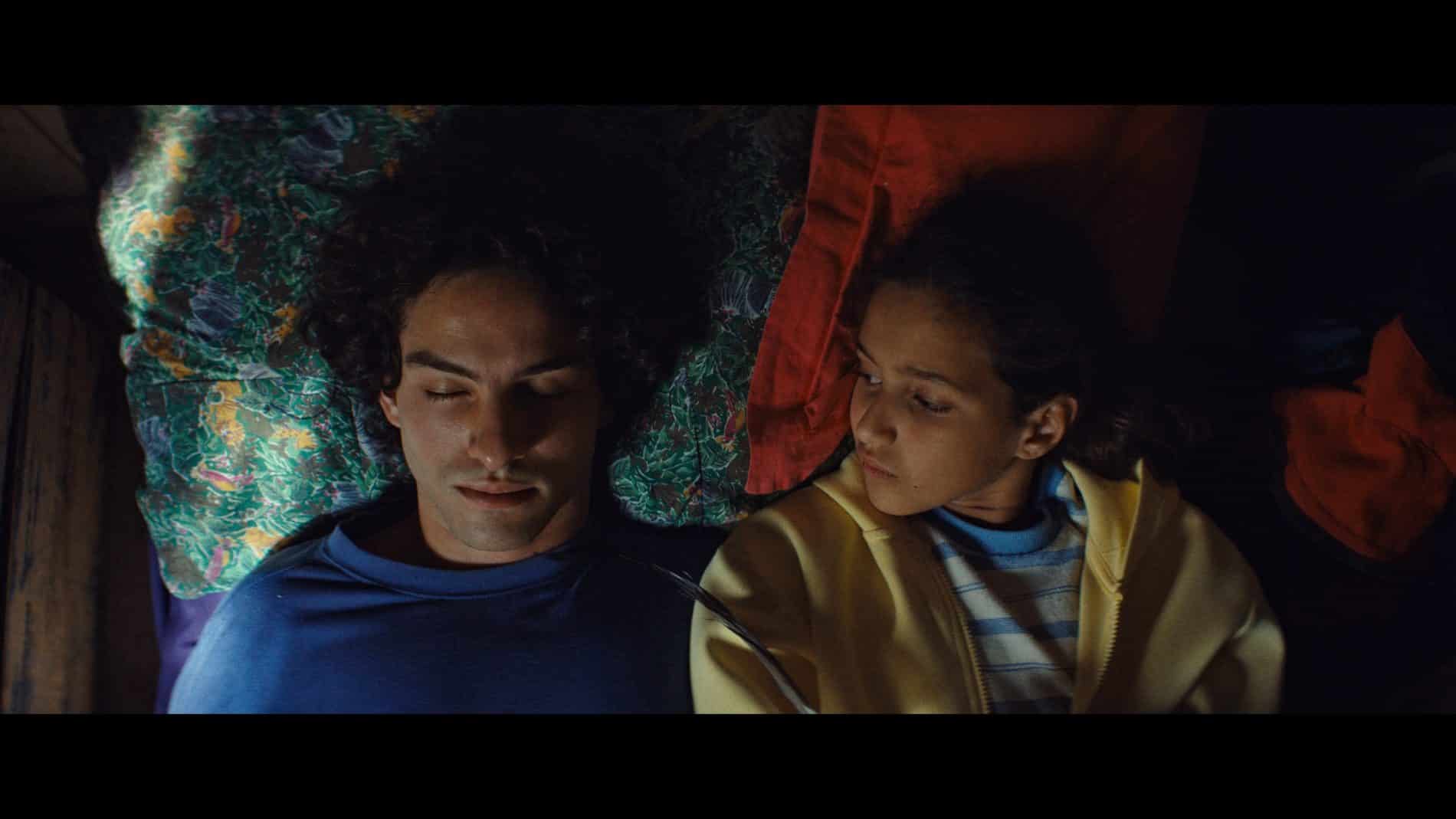 Un jeune homme allongé, les yeux fermés, à côté d’une jeune fille.